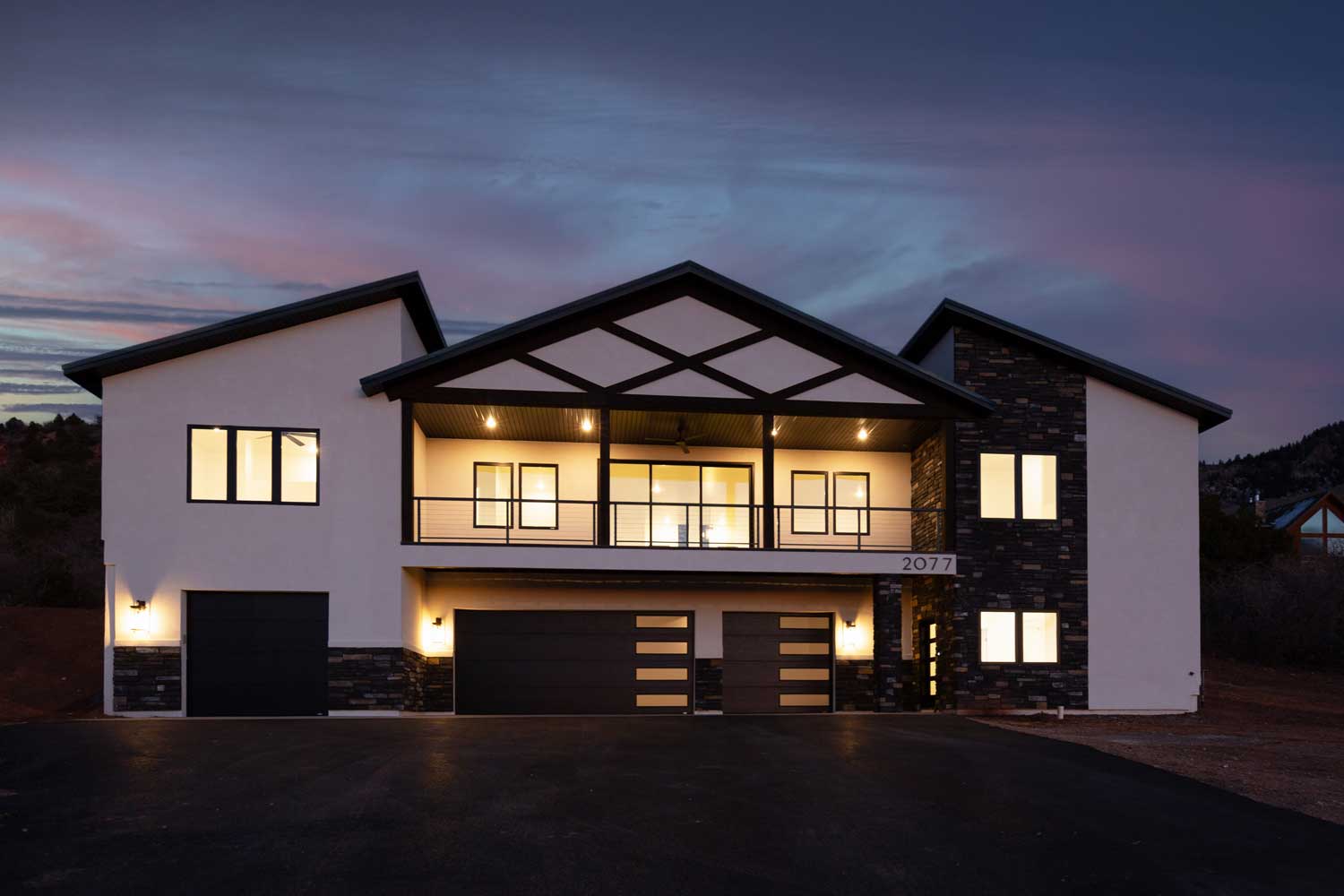 Two story house at night with interior lights on and a blue-pink sky at sunset