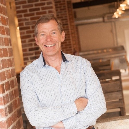 Chris Cipoletti smiling with arms crossed with red brick building in the background